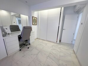 Ein moderner Arbeitsraum mit Schreibtisch, Stuhl und einem großen Spiegel. An der Wand hängt ein gerahmtes Bild, und eine Tür führt in einen anderen Raum.