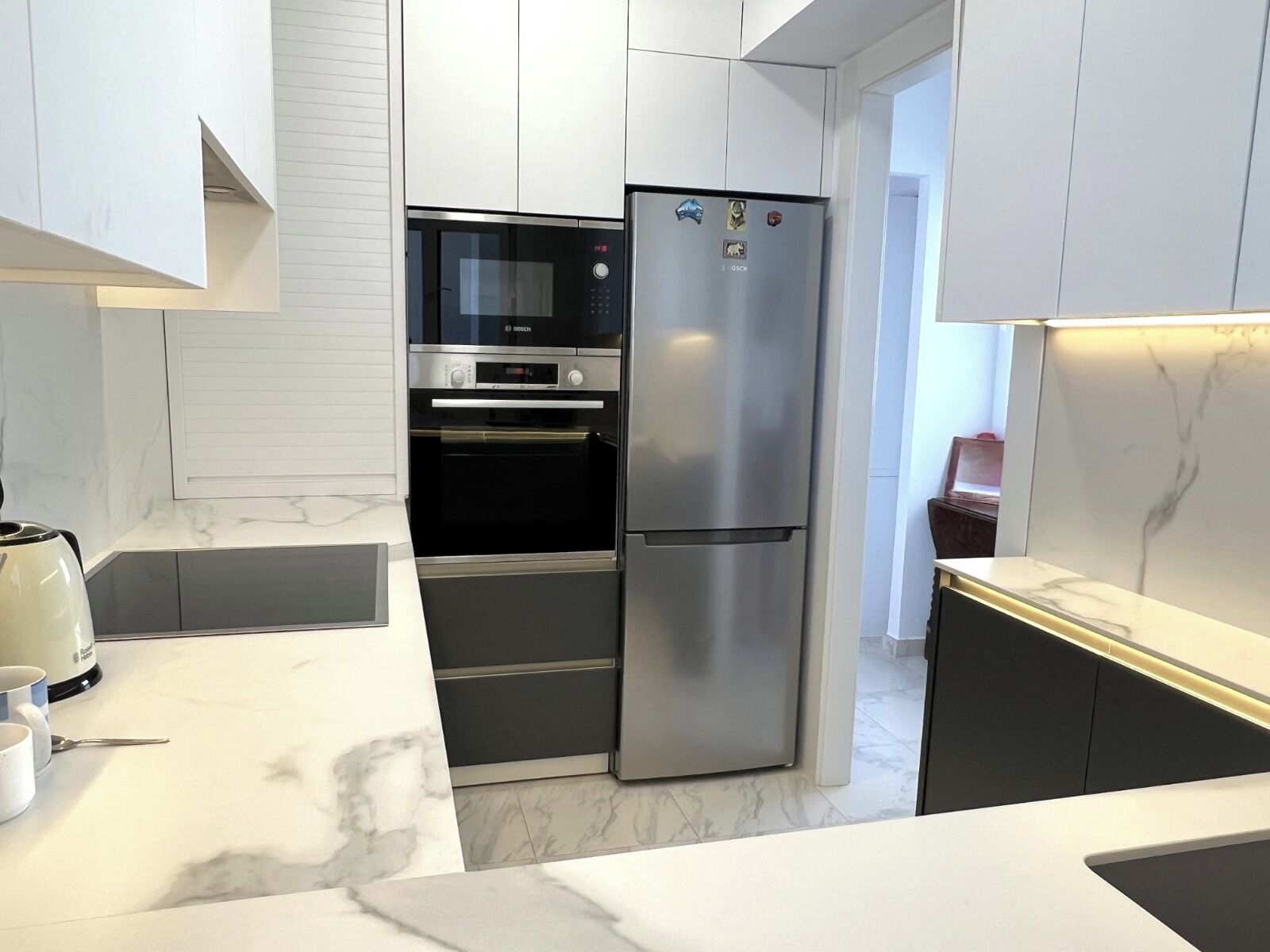 Una cocina moderna con horno empotrado, refrigerador de acero inoxidable y encimera de mármol.