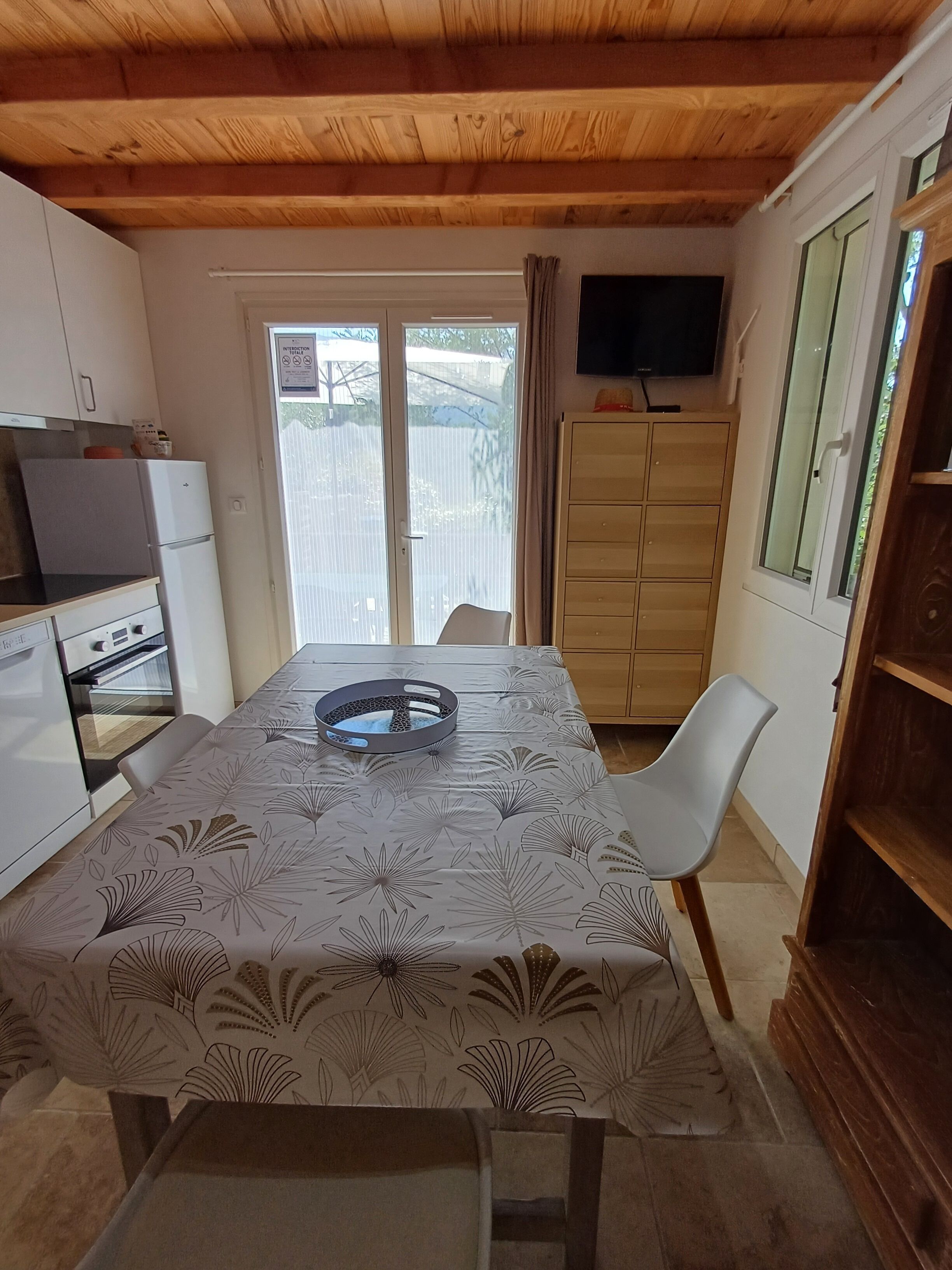 Une cuisine compacte comprenant une table à manger, des chaises, un réfrigérateur, un téléviseur et une porte-fenêtre coulissante donnant sur l’extérieur.