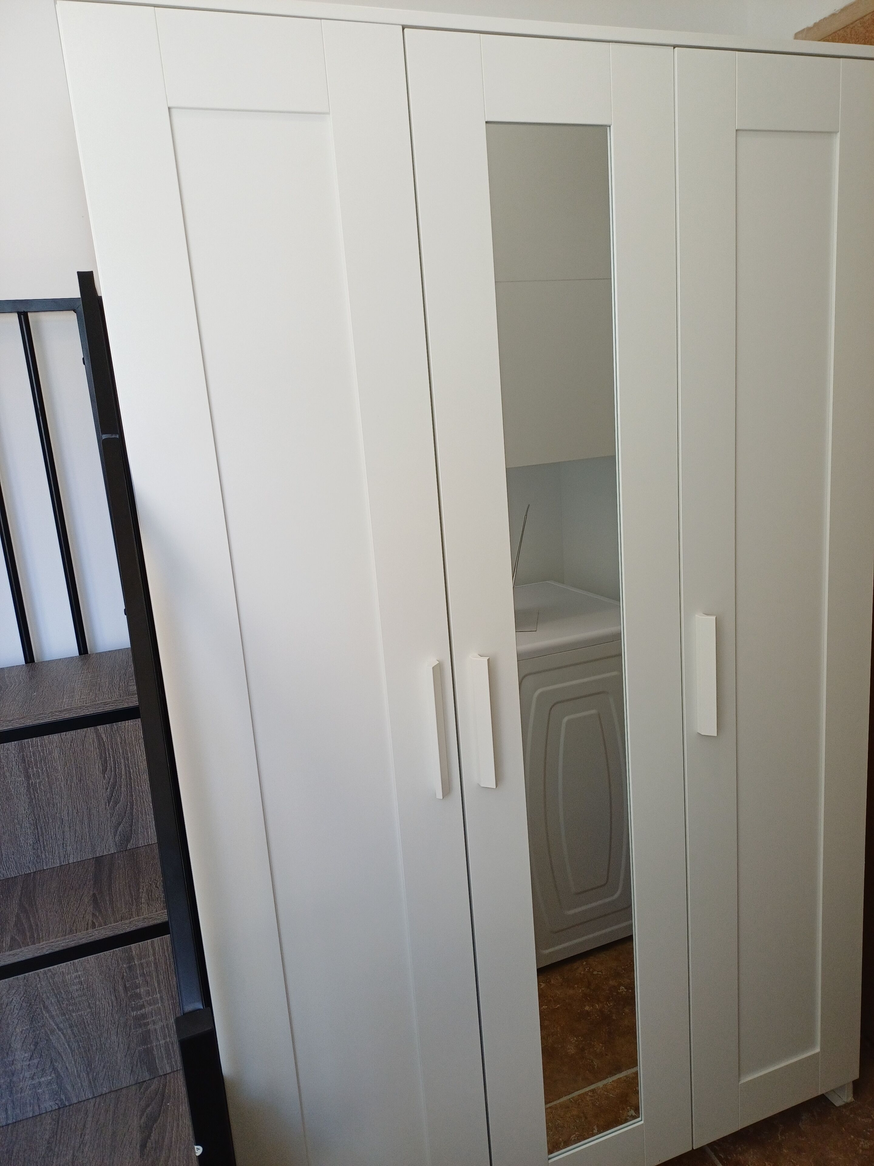 Une armoire blanche à deux portes, dont une partie est recouverte d’un miroir.