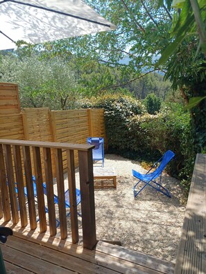 Eine Holzterrasse mit blauem Stuhl und kleinem Tisch, umgeben von einem Holzzaun und üppigem Grün.