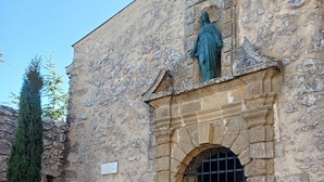 A stone building with a statue above a doorway, a cobblestone path, and a tall evergreen tree. - Victor's House at the Foot of Sainte Victoire (Vauvenargues)