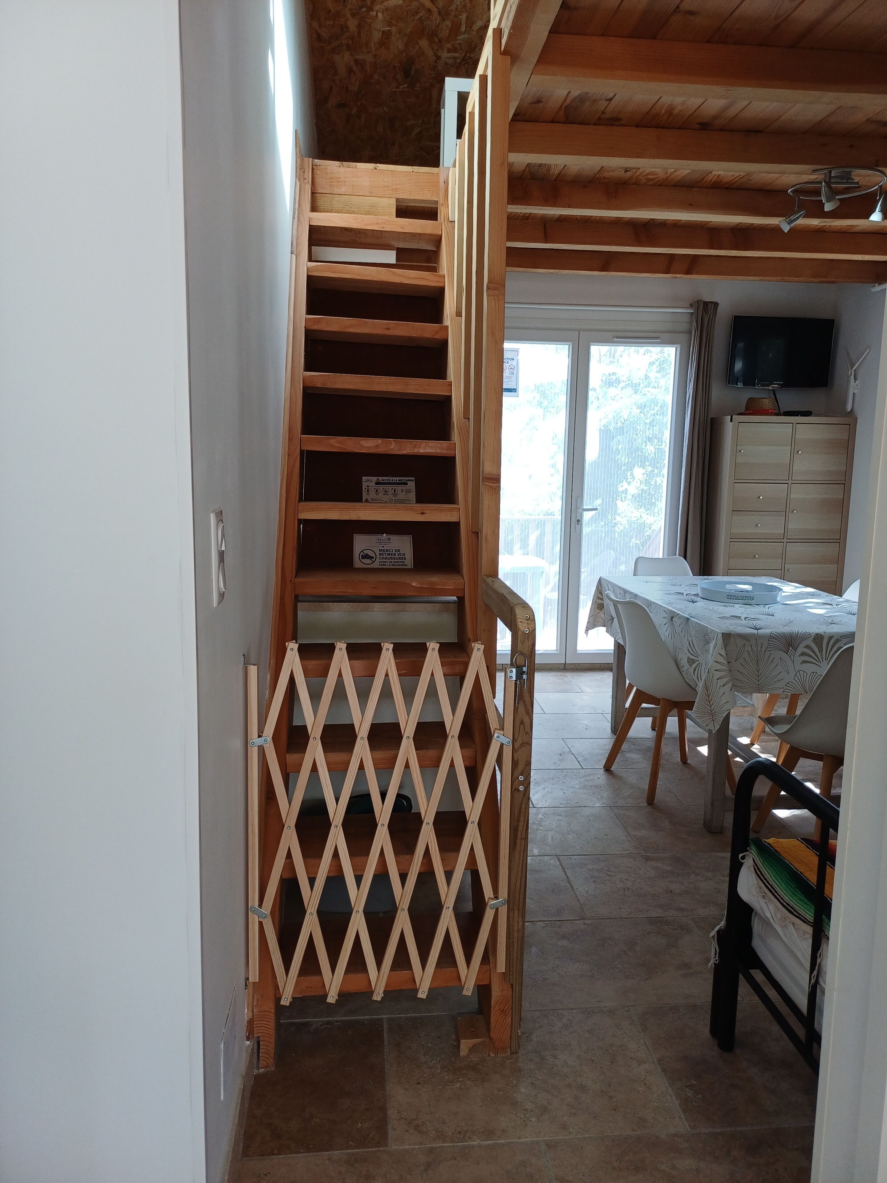 Un escalier avec une rampe en bois menant à un balcon, une table à manger avec des chaises et un téléviseur fixé au mur.