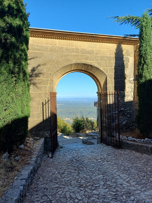 A stone archway leading to a paved path with a view of distant hills.