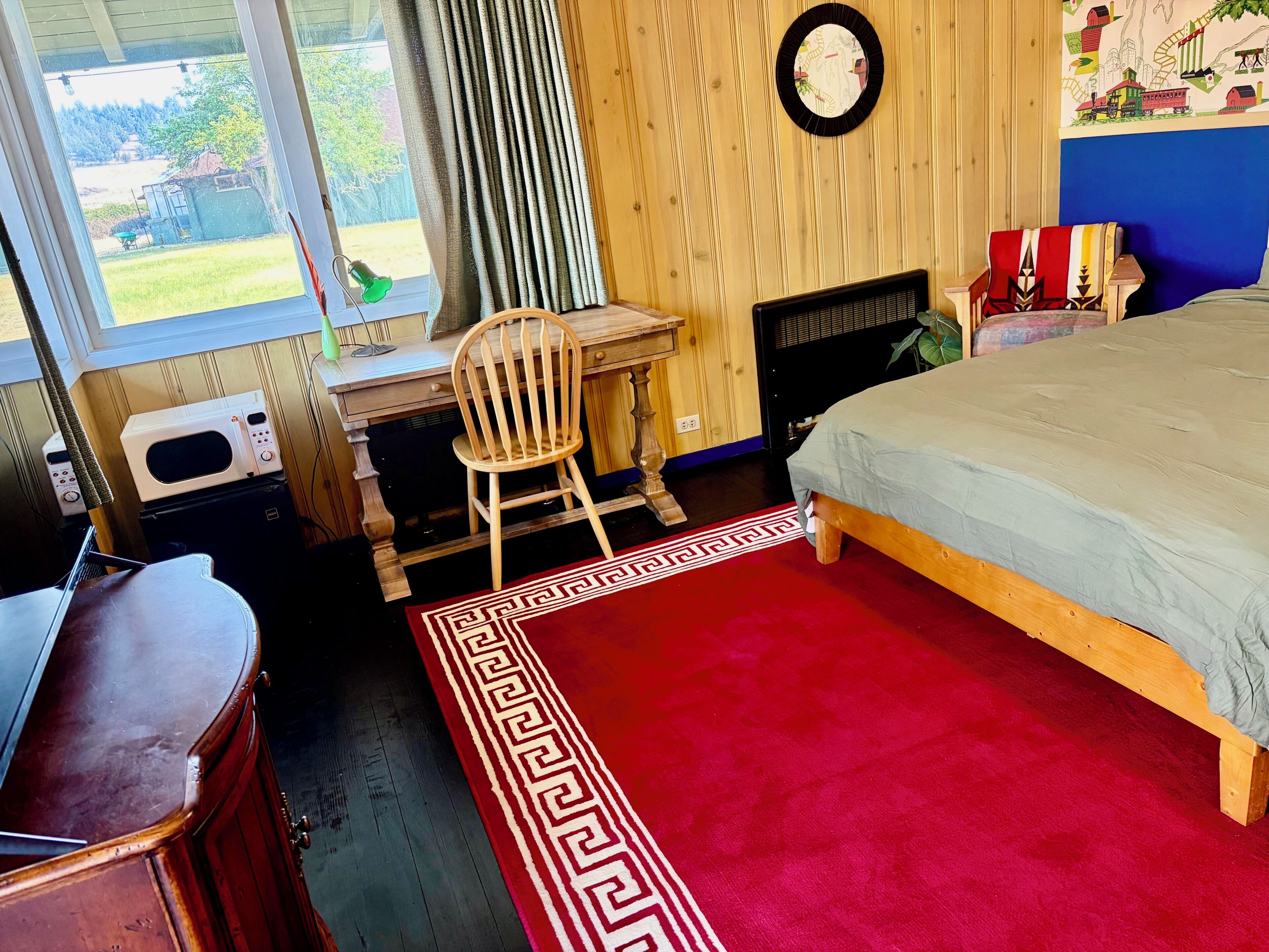 Une chambre à coucher comprenant un lit, un bureau, une chaise, une commode et une fenêtre avec des rideaux.