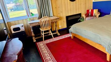 A bedroom with a bed, a desk, a chair, a dresser, and a window with curtains.