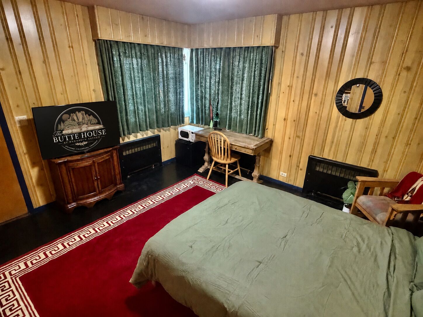 A hotel room with a bed, a desk, a chair, a television, and a red carpet.