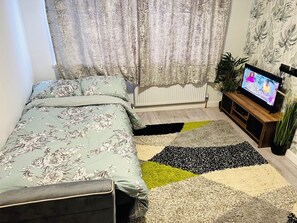 Un dormitori amb llit, televisió, radiador i una catifes amb dibuixos.