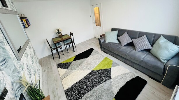 Una sala de estar con un sofá gris, una mesa de comedor con sillas y un tapete estampado.