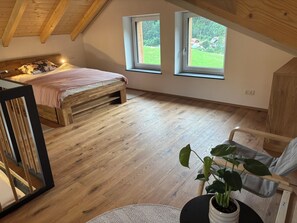 A bedroom with a wooden bed, two windows, a plant, and a chair.