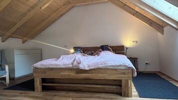 Ett sovrum med ett sluttande tak, en säng i trä, ett sängbord och en lampa.
