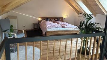 Een slaapkamer met een schuine kap, een bed, een stoel en een klein tafeltje.