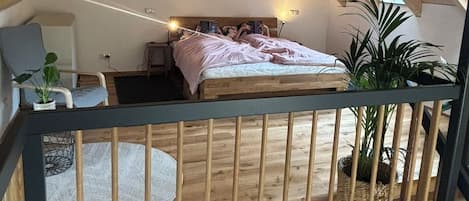 A bedroom with a sloped ceiling, a bed, a chair, and a small table.
