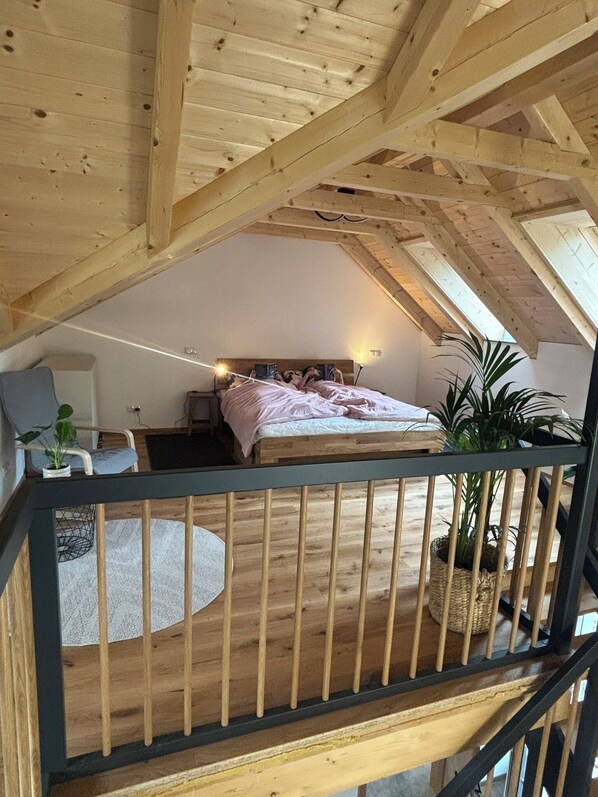 A bedroom with a sloped ceiling, a bed, a chair, and a small table.