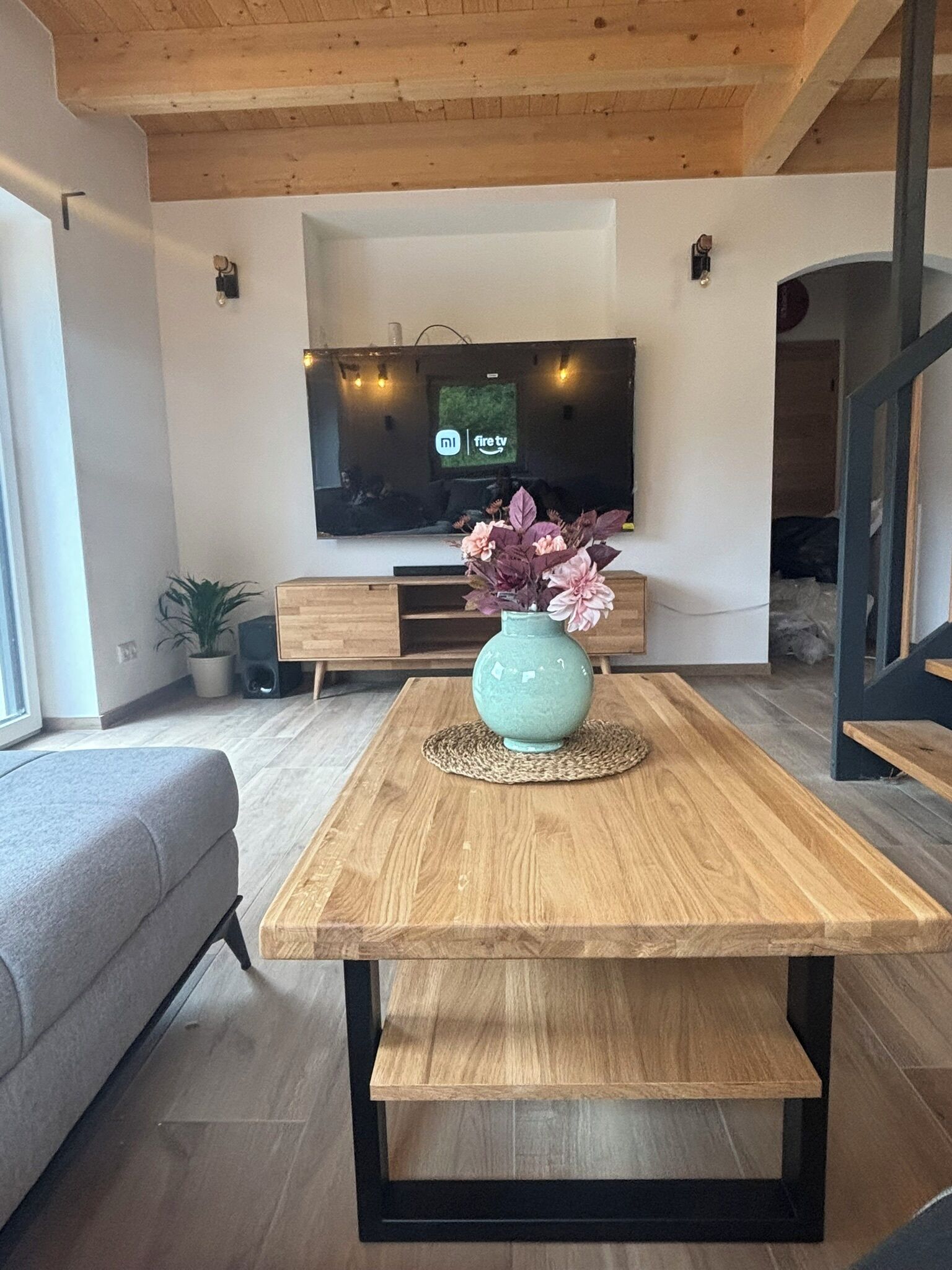 Ein modernes Wohnzimmer mit Holztisch, Sofa, Flachbildfernseher und Topfpflanze.