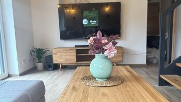 Ein modernes Wohnzimmer mit Holztisch, Sofa, Flachbildfernseher und Topfpflanze.