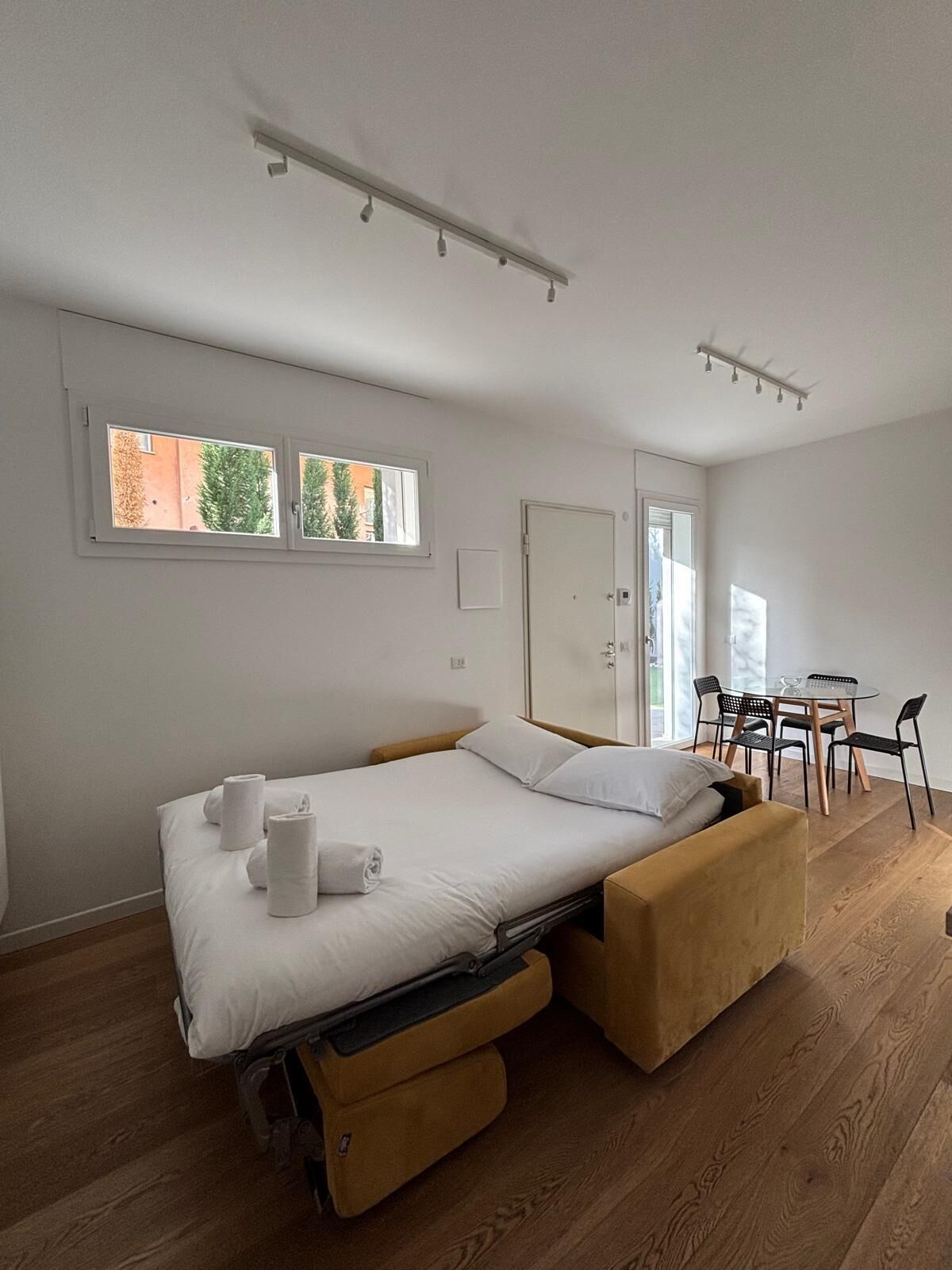Ein modernes Schlafzimmer mit Bett, Nachttischen, einer Schlafcouch, einem Esstisch mit Stühlen und einem Fenster mit Aussicht.