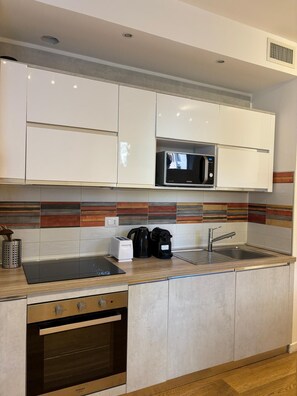 A modern kitchen with white cabinets, a microwave, a toaster, a kettle, and a sink. - Apartment with a private garden and a private parking space (Roma)