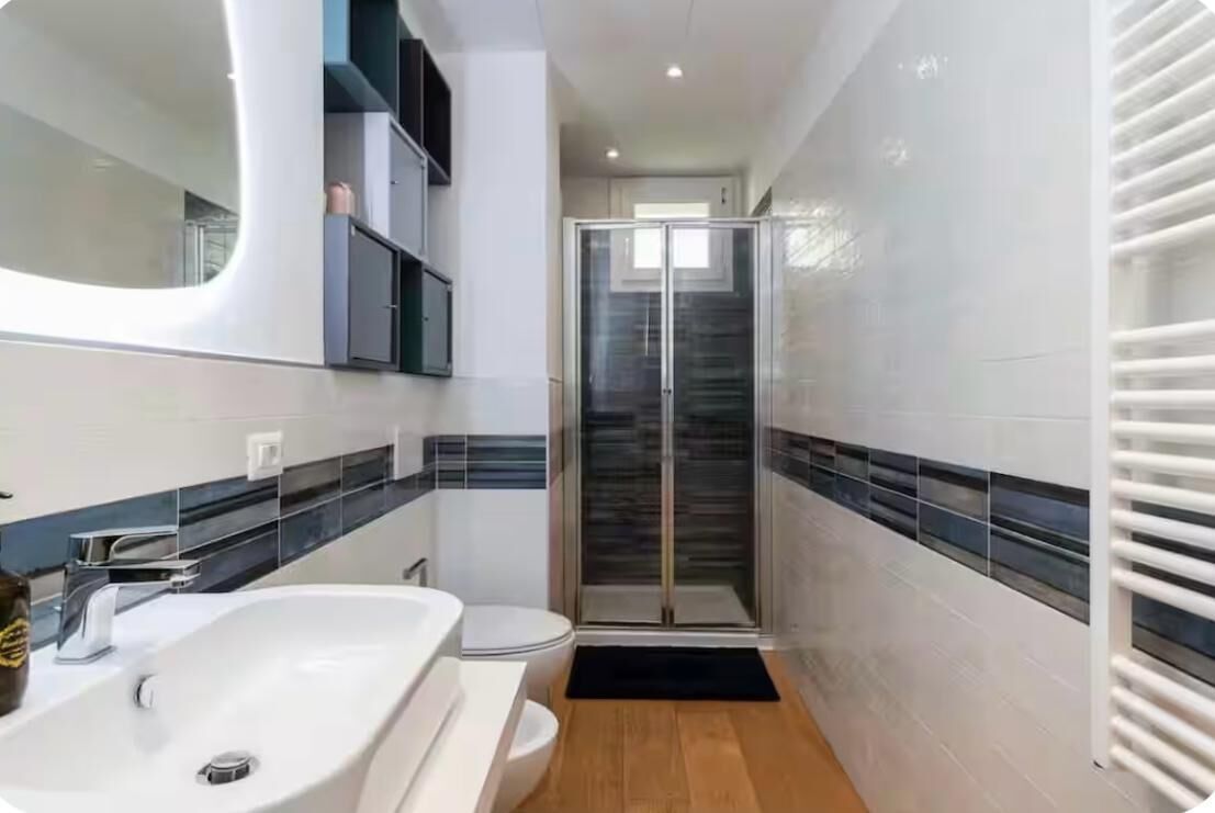 A modern bathroom with a white sink, toilet, and a glass-enclosed shower.
