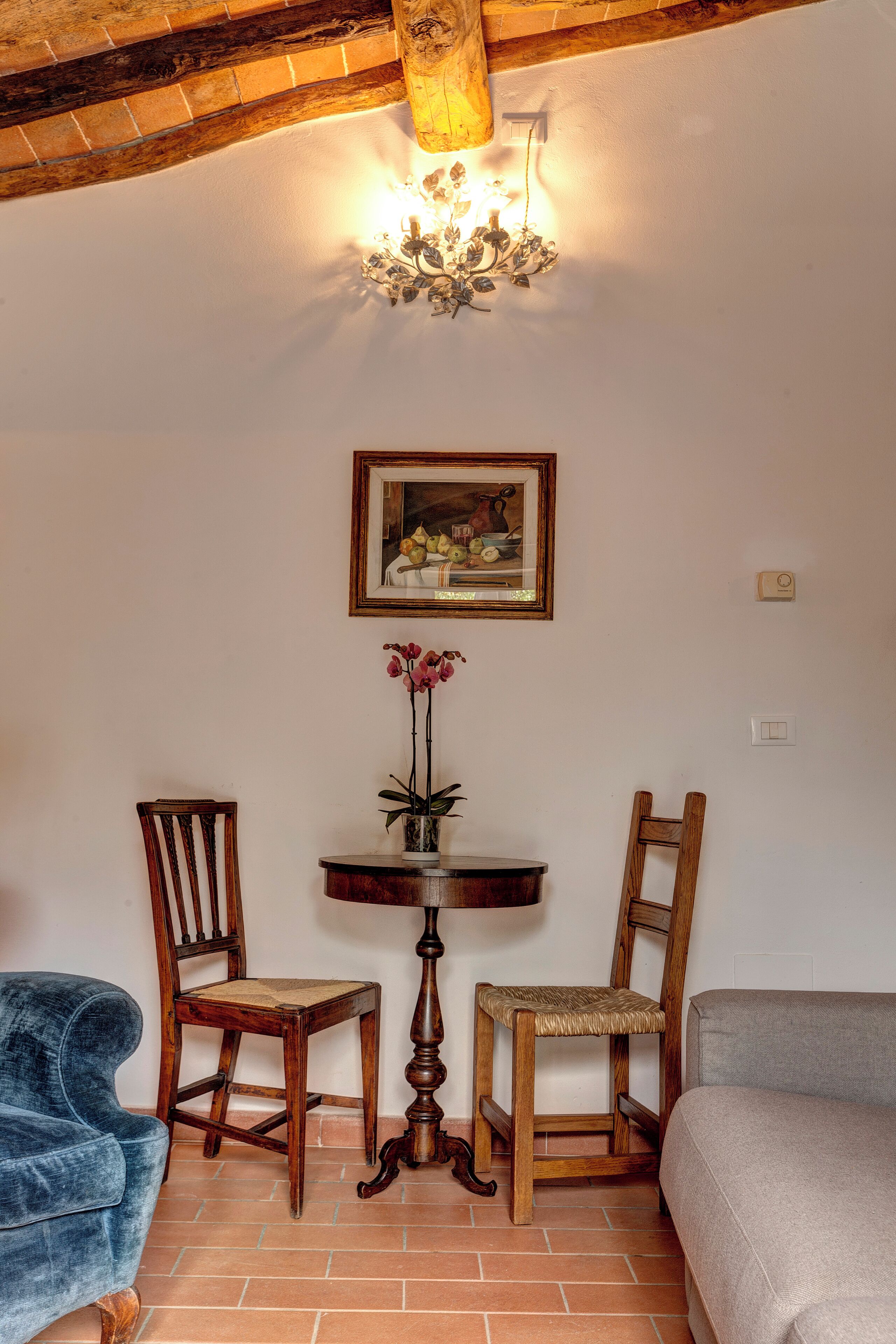 A room with a wooden table, two chairs, a painting, and a chandelier.