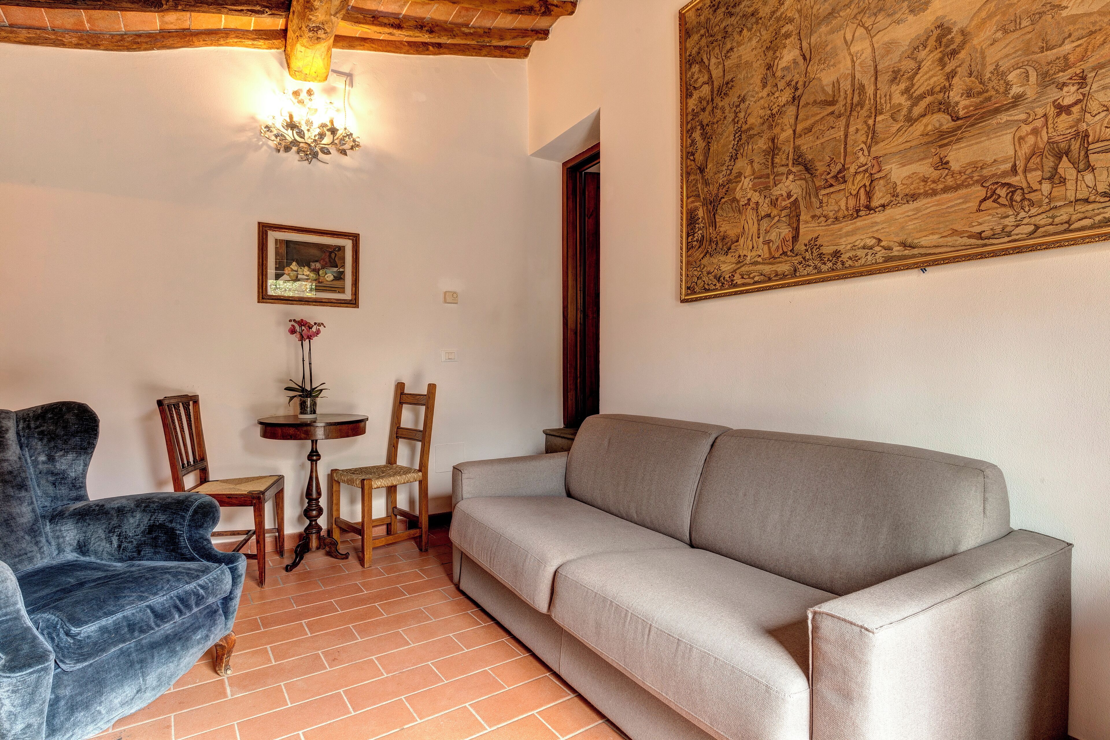 A living room with a sofa, chairs, a small table with a plant, and a painting on the wall.