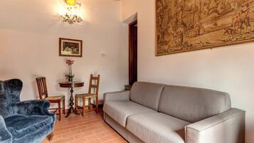 A living room with a sofa, chairs, a small table with a plant, and a painting on the wall.