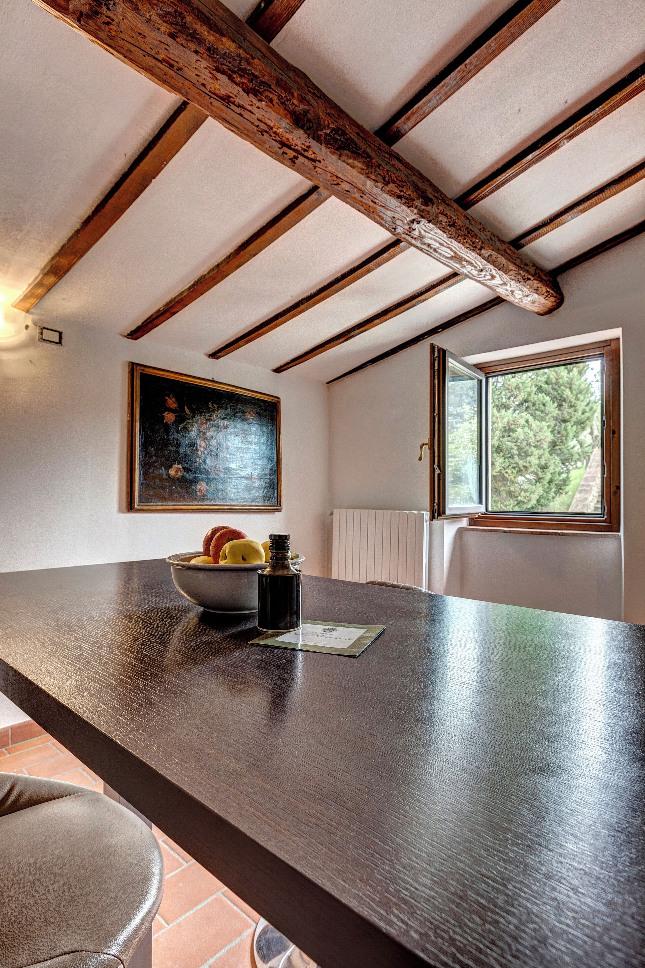 Una cocina con mostrador de madera, un tazón de fruta, una botella y una ventana con vistas a árboles.