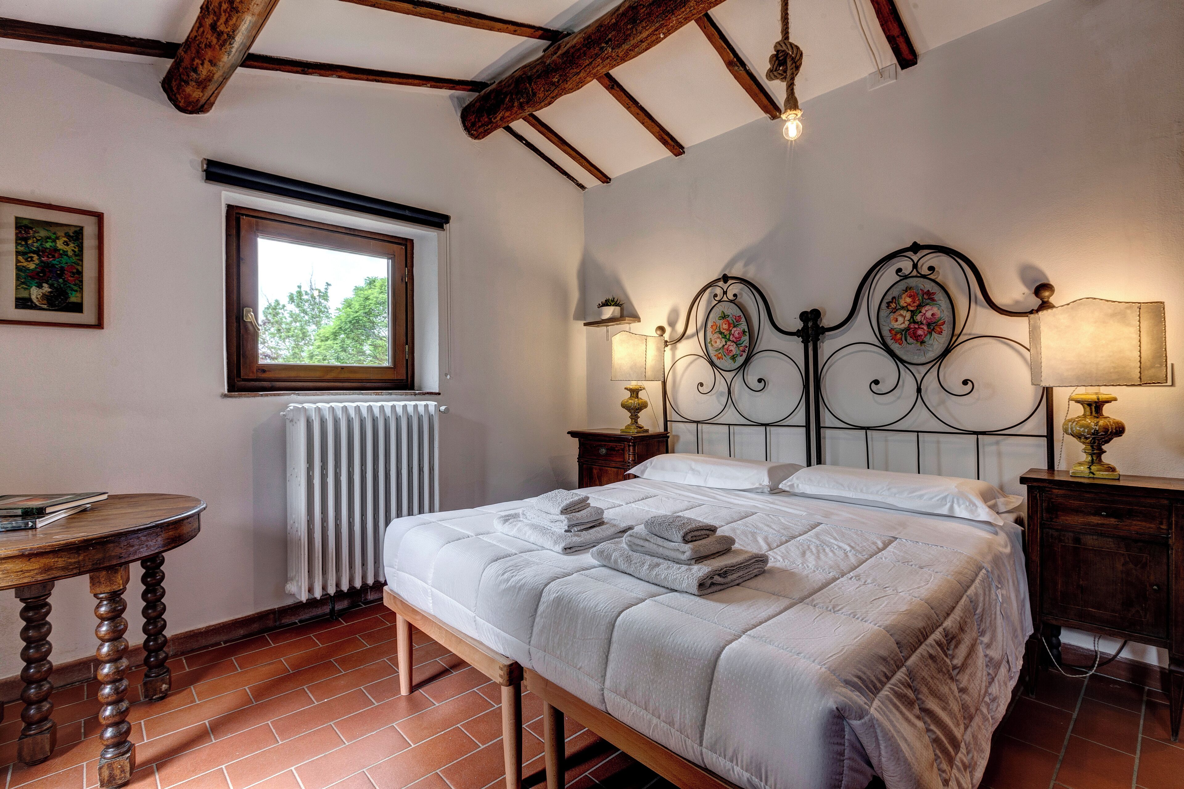 Une chambre à coucher avec un lit, des tables de chevet, une fenêtre, un radiateur et un banc en bois.