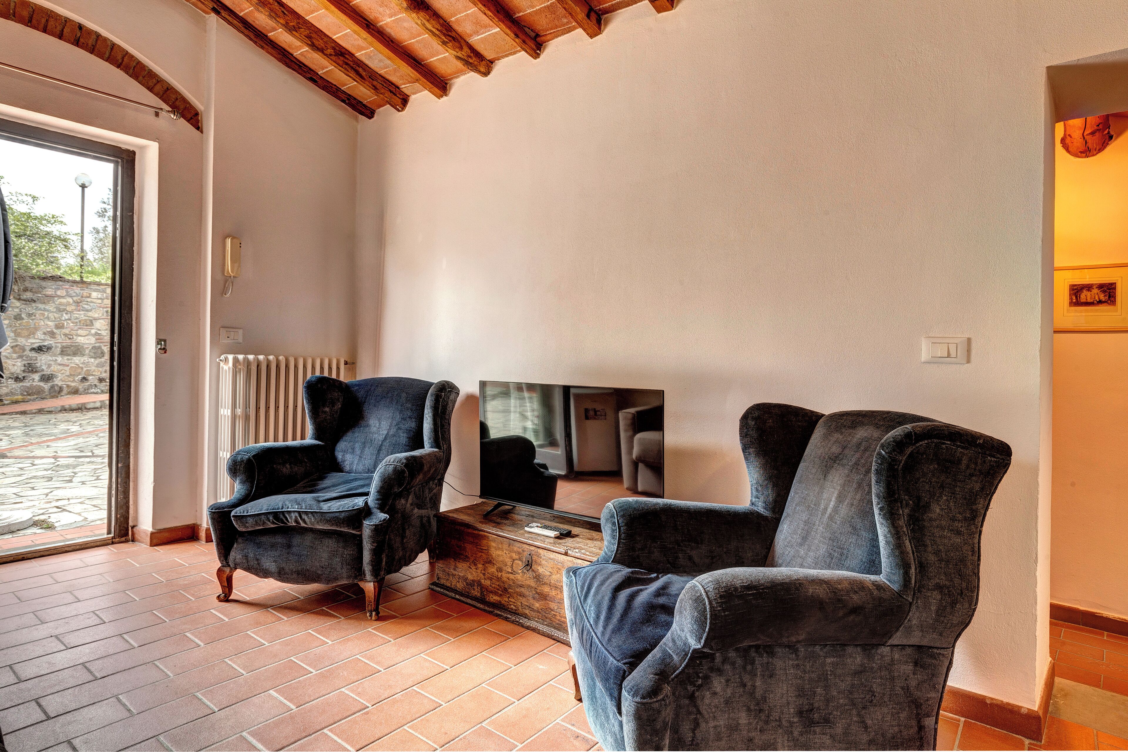 Une pièce comprenant deux fauteuils, une table basse en bois, un téléviseur et une porte donnant sur l’extérieur.