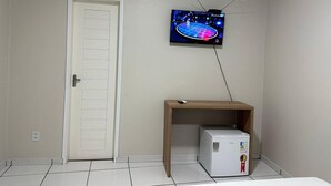 Una habitación con una puerta blanca, una pequeña mesa de madera y un electrodoméstico blanco, además de un televisor montado en la pared.