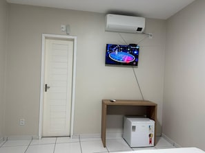 Una habitación con una puerta blanca, una pequeña mesa de madera y un electrodoméstico blanco, además de un televisor montado en la pared.