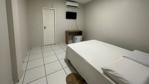 Un dormitorio con una cama, un televisor montado en la pared y una mesita con un calentador.