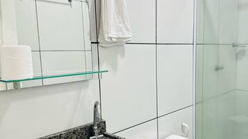 Casa de banho com lavatório bancada de granito, sanita, cabine de duche em vidro e espelho com toalheiro.
