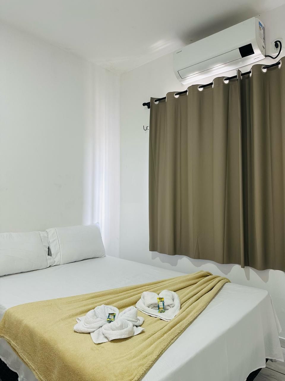 Una habitación de hotel con una cama, una colcha color beige, dos toallas blancas y una ventana con cortinas.
