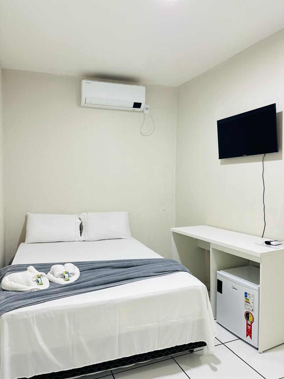 Habitación de hotel con cama, televisor montado en la pared, escritorio pequeño y refrigerador.