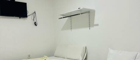 A hotel room with two beds, a flat-screen TV mounted on the wall, and a small shelf above the beds.