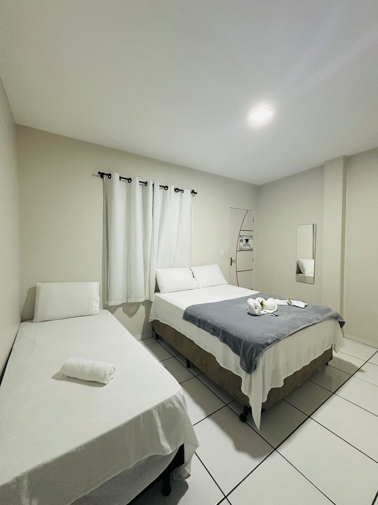 Habitación de hotel con dos camas, baño con espejo y suelo de baldosas.