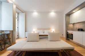 Un dormitorio moderno con cama, lámparas de noche, una mesita y una kitchenette.