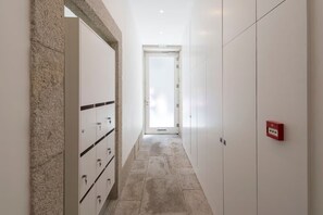 A hallway with lockers, a door at the end, and a red emergency light. - Rico's Apartment 1B - Prime Location in Central Porto (Porto)