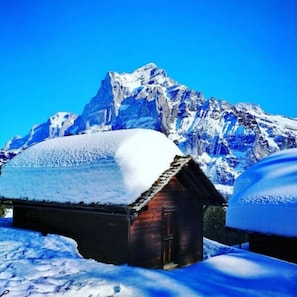 A snow-covered mountain with a wooden cabin in the foreground.