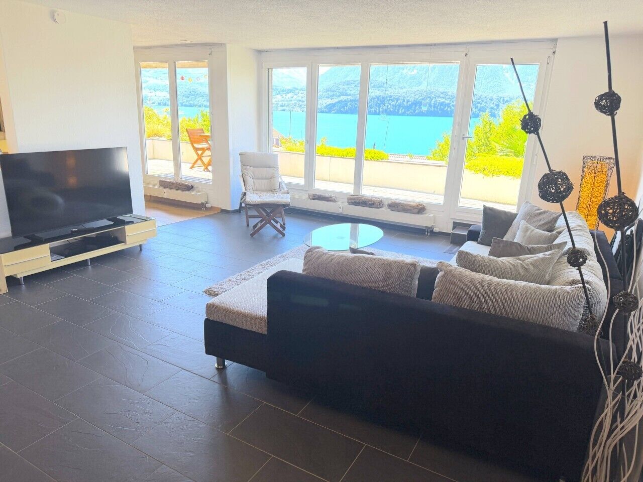 Un salon moderne avec un grand canapé, un téléviseur à écran plat et une vue sur un lac, grâce à de grandes fenêtres.