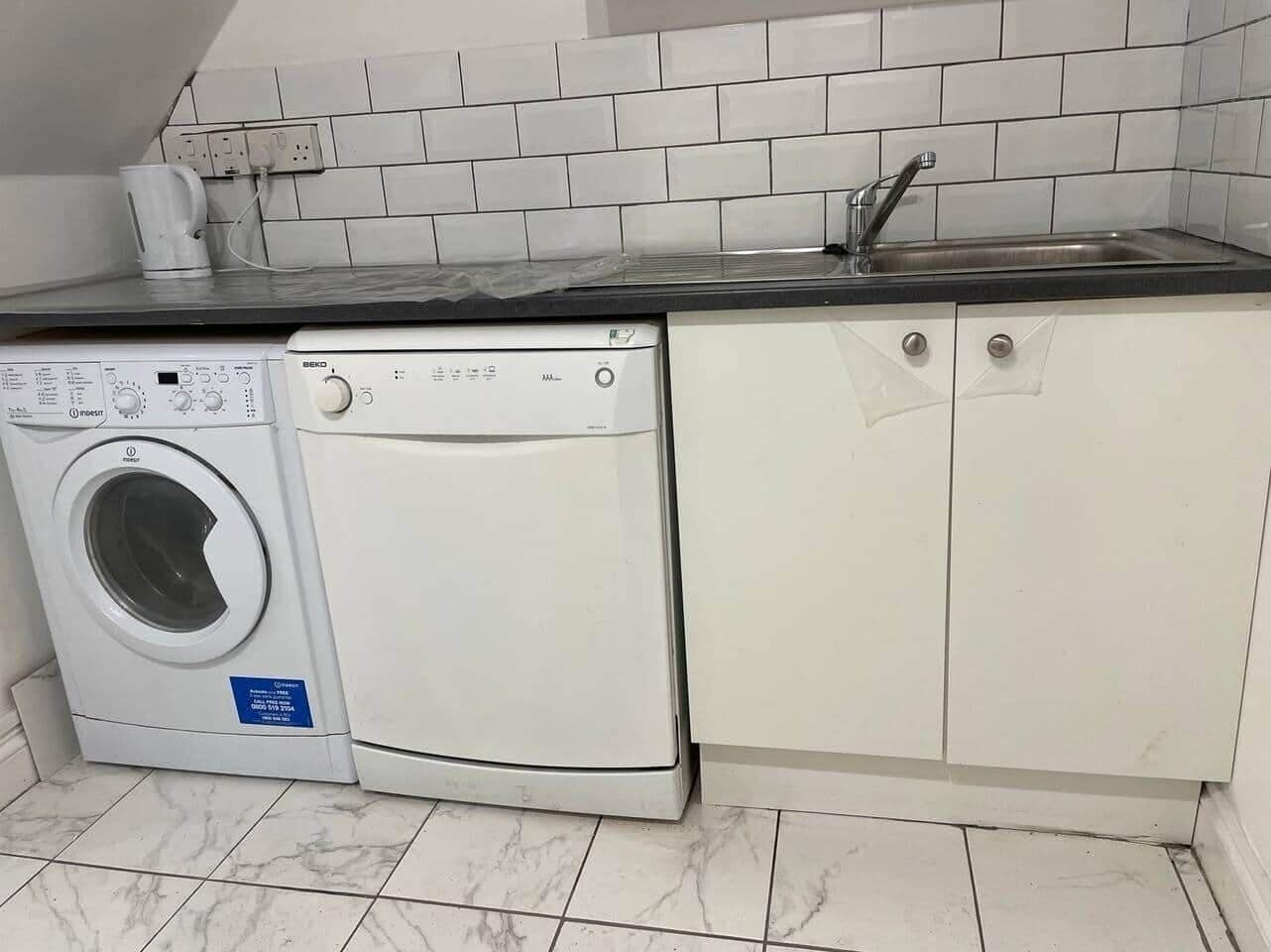 A compact kitchen with a washing machine, a sink, and white cabinets.