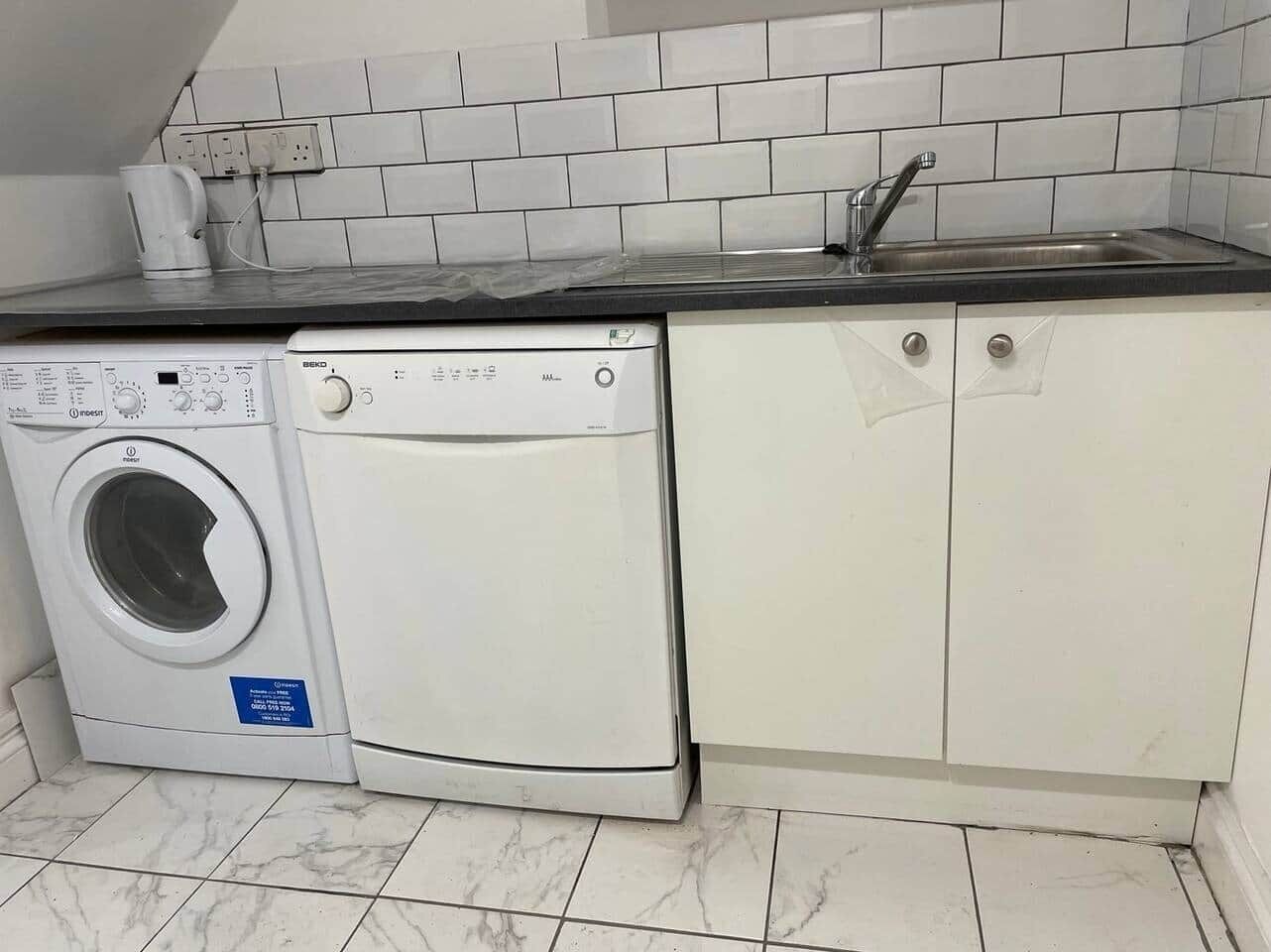A compact kitchen with a washing machine, a sink, and white cabinets.