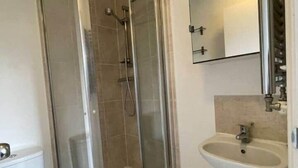 Een badkamer met een douchecabine van glas, een witte wastafel en een toilet.