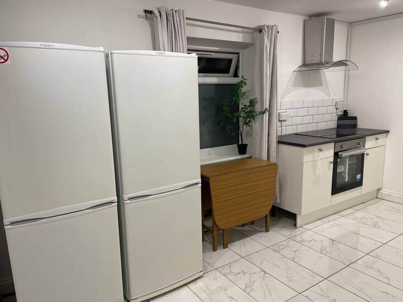 Ett kompakt kök med kylskåp, ugn och ett litet matbord.