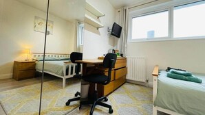 Een slaapkamer met een bed, een bureau, een stoel, een dressoir, een spiegel, een raam en een radiator.