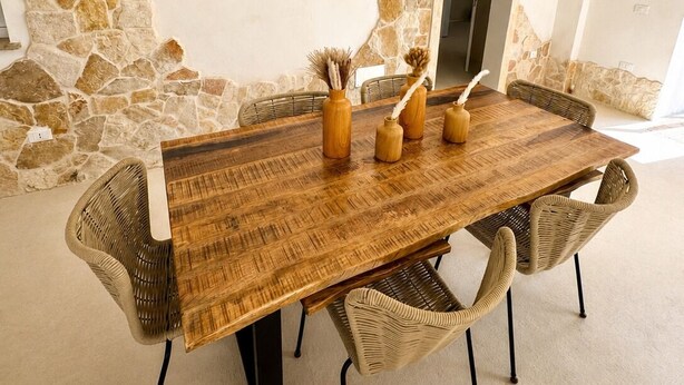 Un coin repas avec une table en bois et des chaises en osier, un mur en pierre et une porte.