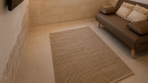 Une pièce avec un plafond en bois, un téléviseur à écran plat fixé au mur, une fenêtre donnant sur un beau paysage, un canapé marron avec des coussins et un tapis tissé sur le sol.