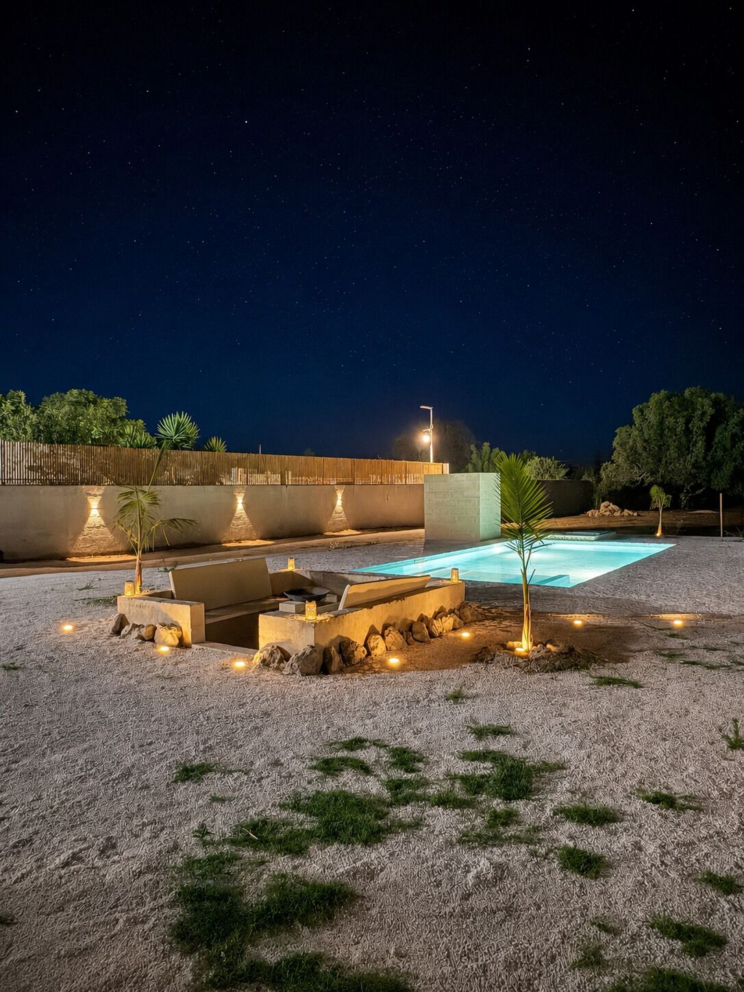 A nighttime outdoor area with a swimming pool, stone seating, and a starry sky.