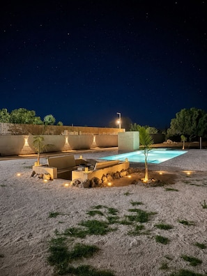 A nighttime outdoor area with a swimming pool, stone seating, and a starry sky.